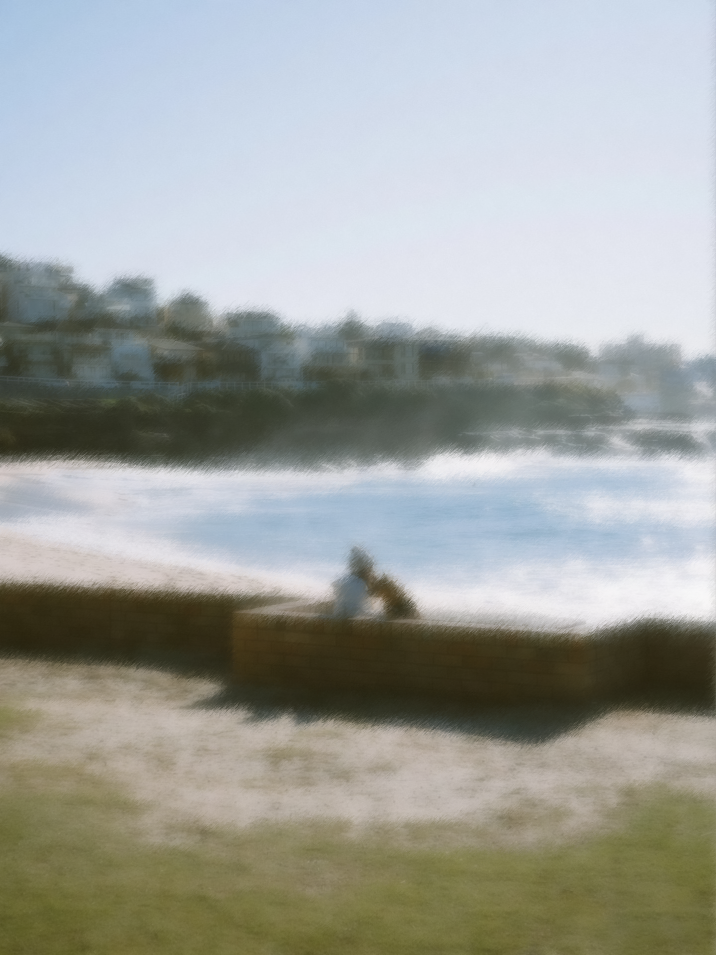 A soft-focus seaside scene with two figures sitting together near the shore